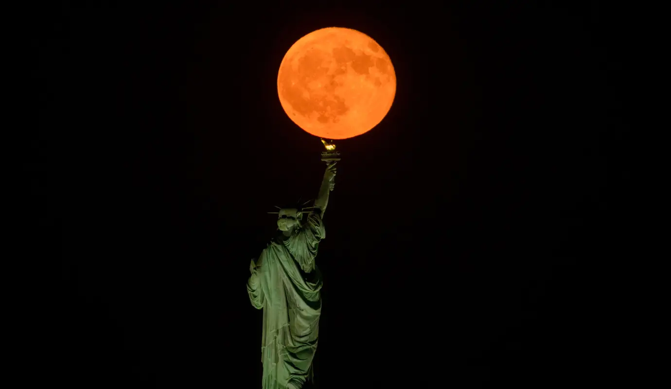 La Luna llena del esturión sale detrás de la Estatua de la Libertad en la ciudad de Nueva York. Foto: GETTY