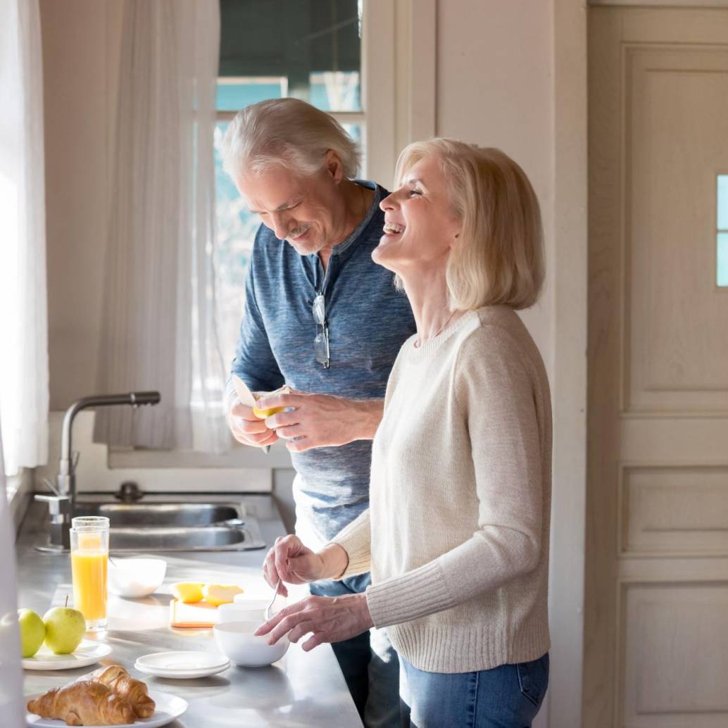 Happy loving senior couple having fun preparing healthy food on breakfast in the kitchen, mature smiling man and woman laughing cooking together on weekend morning, aged old family at home concept