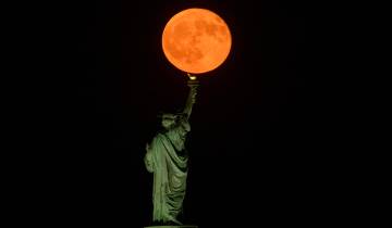 La Luna llena del esturión sale detrás de la Estatua de la Libertad en la ciudad de Nueva York. Foto: GETTY