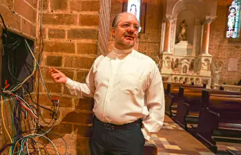 El padre Leonardo muestra el enjambre de alambres que tocó cambiar en la red eléctrica. El enverjado es necesario para quitar el zócalo y corregir la humedad así como para controlar a quienes dañan las paredes y se orinan en las afueras. FOTO MANUEL SALDARRIAGA