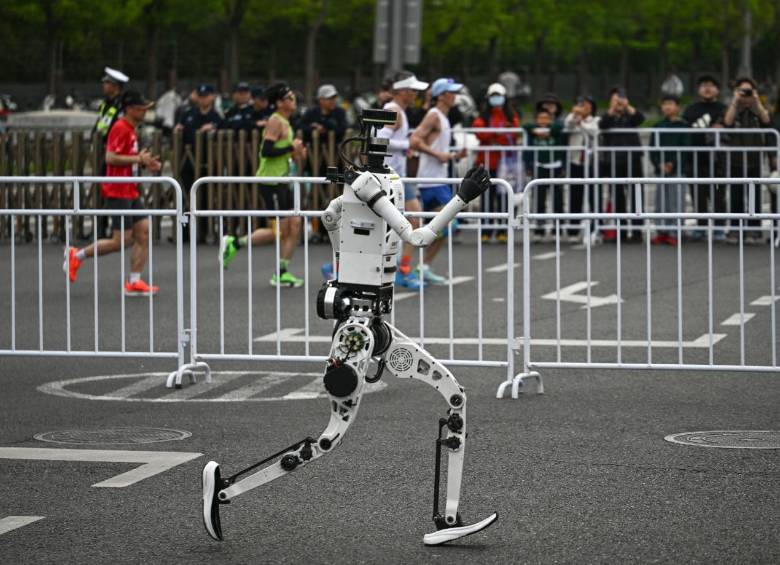 En un carril, uno de los robots humanoides participantes, en el otro, las personas corriendo la media maratón de Pekín. FOTO AFP. 
