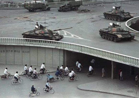 AP - 6 de junio 1989. Ciclistas pasan frente a grafitis que dec&#237;an &quot;movilizar a todos los ciudadanos para aplastar la ley marcial, proteger Beijing&quot;, debajo de un puente donde veh&#237;culos blindados tomaban posici&#243;n en Changan Blvd.