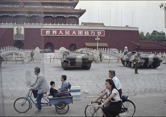 AP - 13 de junio de 1989. Gente en bicicleta pasan frente a varios veh&#237;culos blindados estacionados en frente de la puerta de Tiananmen.