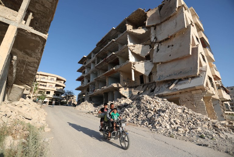 Syrian men ride a motorcycle past heavily-damaged buildings in the rebel-held town of Maaret al-Numan, in the north of Idlib province on September 27, 2018. OMAR HAJ KADOUR / AFP
