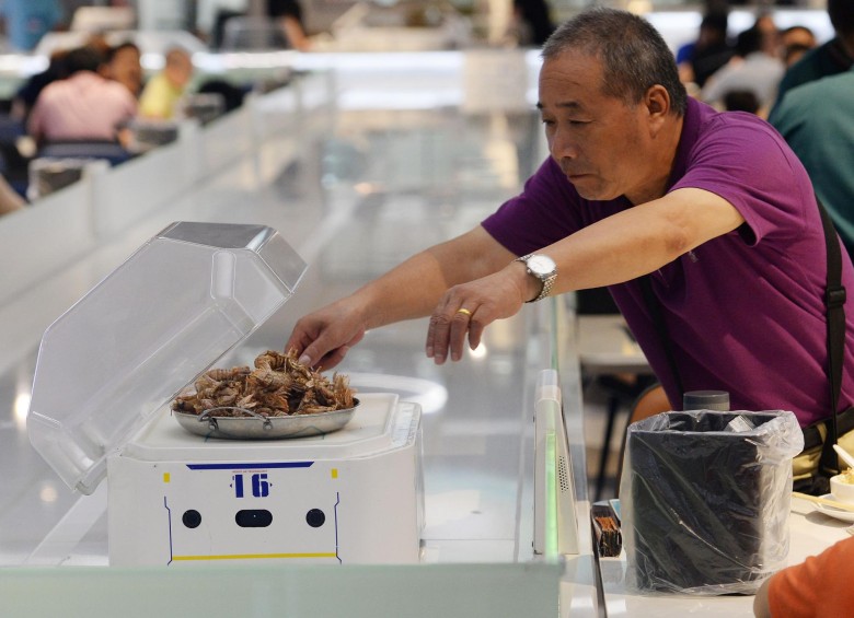 El pequeño mesero robótico rueda hacia la mesa, levanta la tapa de vidrio para revelar el humeante plato de cangrejos al estilo de Shanghai. FOTOS: AFP