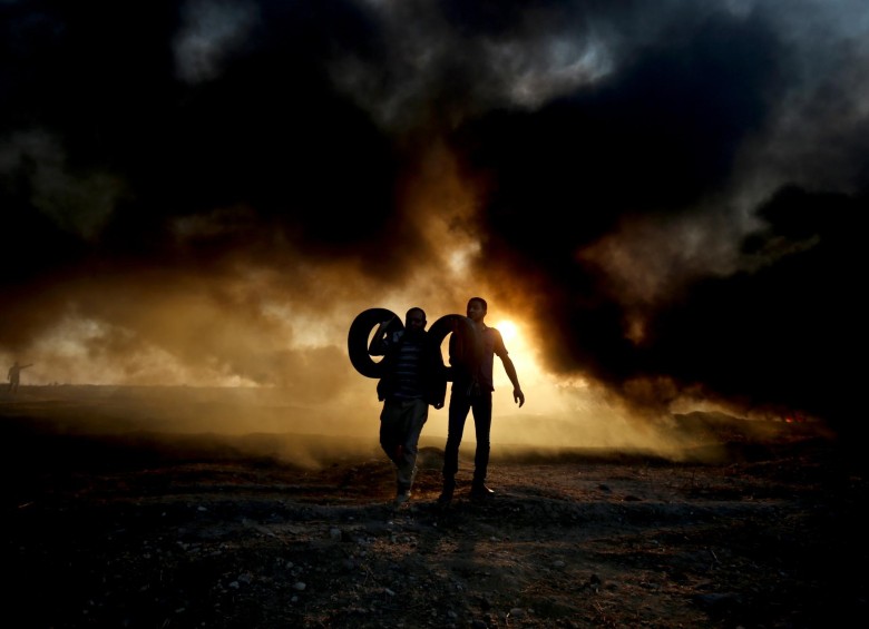 Manifestantes palestinos sostienen unas llantas mientras el humo emana de los neumáticos quemados en la frontera de Gaza con Israel FOTO AFP