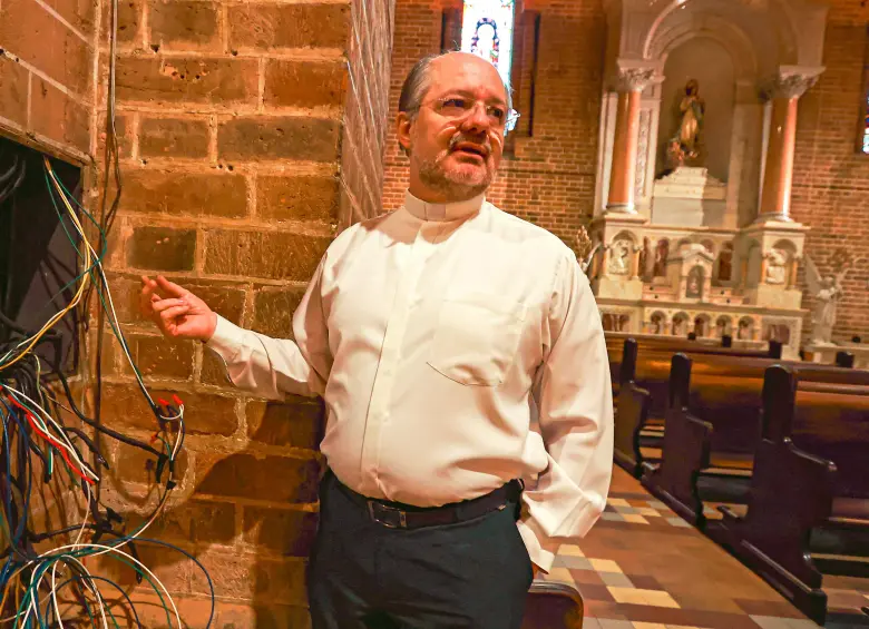 El padre Leonardo muestra el enjambre de alambres que tocó cambiar en la red eléctrica. El enverjado es necesario para quitar el zócalo y corregir la humedad así como para controlar a quienes dañan las paredes y se orinan en las afueras. FOTO MANUEL SALDARRIAGA