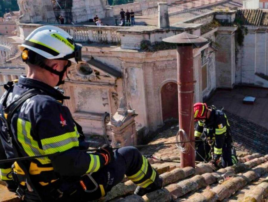 Una brigada de bomberos del Vaticano subió al hastial del tejado de la Capilla Sixtina para instalar la chimenea sin que la mayoría de turistas y fieles en San Pedro lo notara. FOTO: Tomada de X @VaticanNews