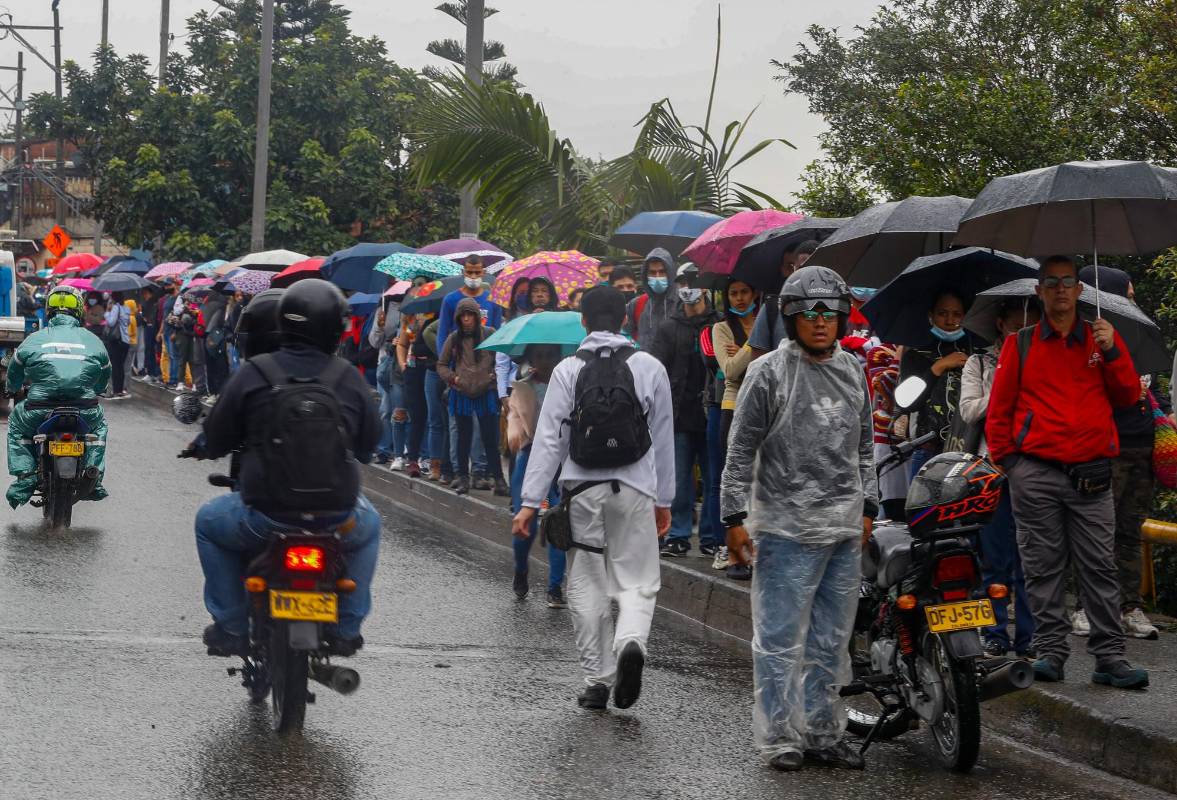 Los usuarios bajo sombrillas, con resignación, en la gris mañana de inicio de semana esperan el transporte que los lleve a la otra estación. Foto: MANUEL SALDARRIAGA QUINTERO.