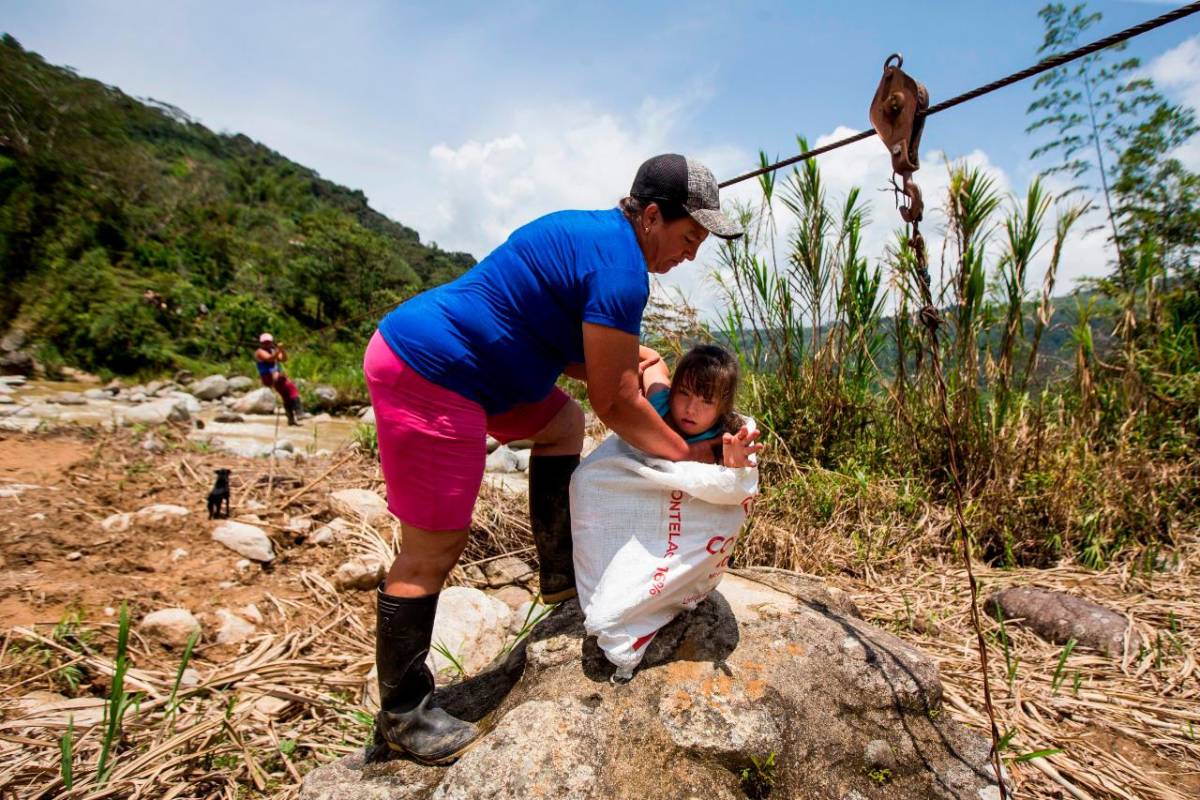Una maniobra riesgosa, una niña es introducida en un costal, luego el costal se enclava en una polea, la niña queda encerrada y un adulto sentado en un lazo que le sirve de sillón carga la niña y se descuelga por una viga metálica para avanzar y pasar al otro lado del río. FOTO JULIO CÉSAR HERRERA