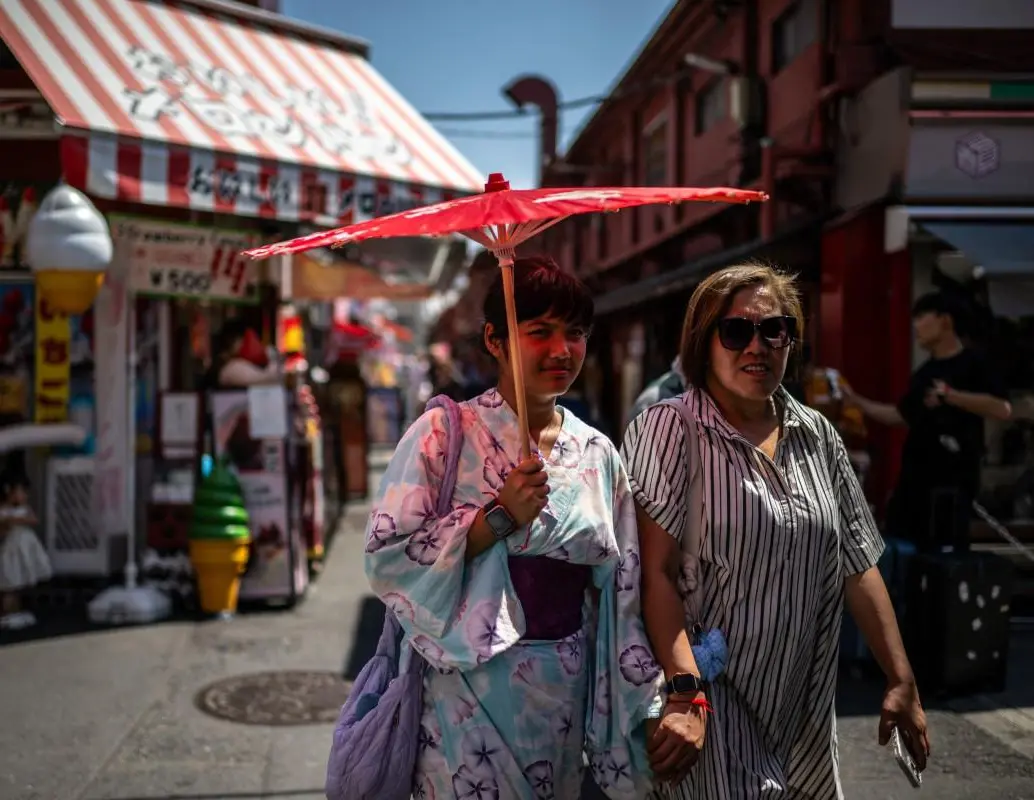 Los turistas comparten un paraguas tradicional para protegerse del sol mientras caminan por una calle comercial en Tokio. FOTO: AFP