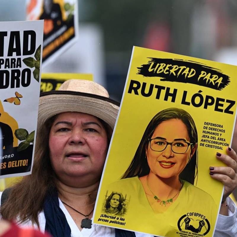 Una mujer lleva fotografías de presos políticos mientras asiste a una protesta contra el Gobierno de Nayib Bukele durante una manifestación. FOTO: AFP