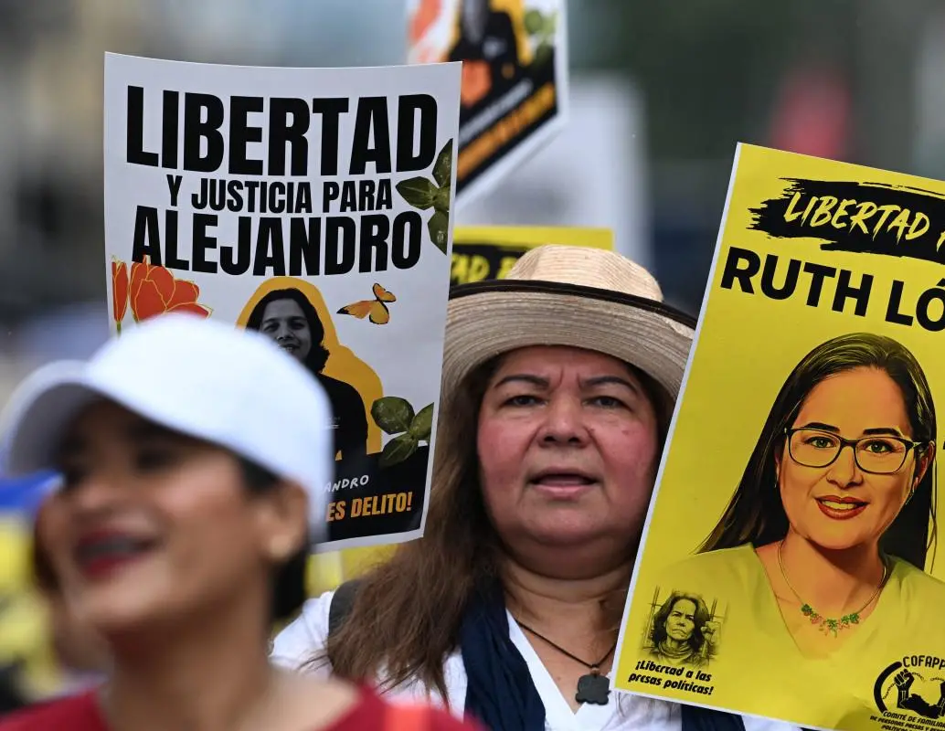 Una mujer lleva fotografías de presos políticos mientras asiste a una protesta contra el Gobierno de Nayib Bukele durante una manifestación. FOTO: AFP