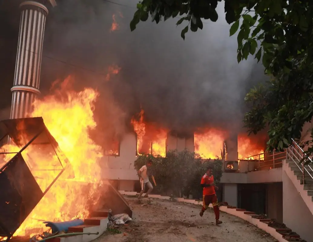 Manifestantes corren junto a las llamas frente a la sede del Partido del Congreso Nepalí incendiada en Katmandú, durante las protestas del 9 de septiembre de 2025 contra la corrupción y la represión policial. FOTO: AFP