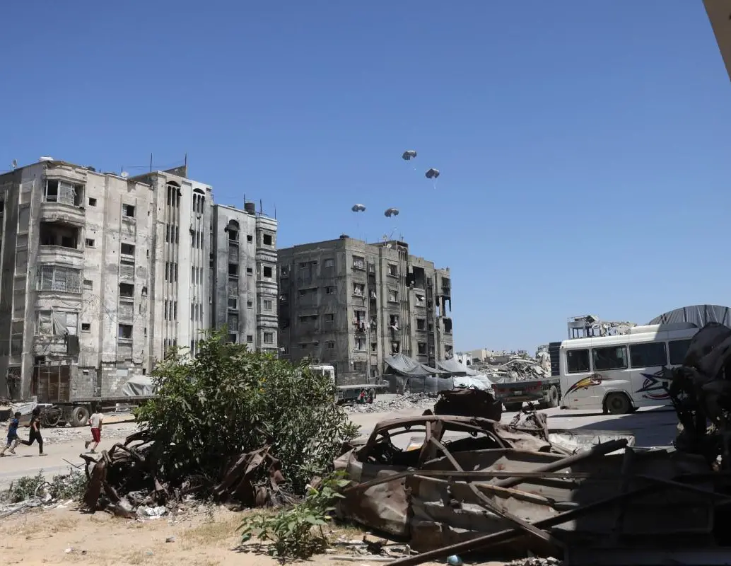 Los palestinos corren hacia paletas de ayuda mientras se lanzan en paracaídas después de ser arrojados desde un avión militar en el norte de la Franja de Gaza. FOTO: AFP