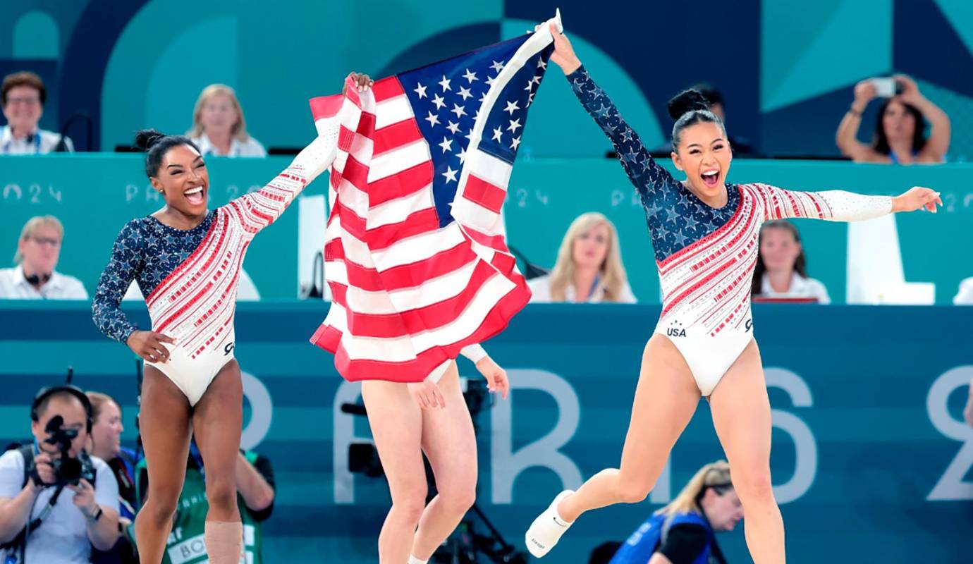 Simone Biles (izq.) del equipo de EE. UU. y Sunisa Lee llevan la bandera estadounidense después de ganar el oro en la final por equipos de gimnasia femenina en el cuarto día de los Juegos Olímpicos de París 2024. Foto: GETTY