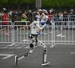En un carril, uno de los robots humanoides participantes, en el otro, las personas corriendo la media maratón de Pekín. FOTO AFP.