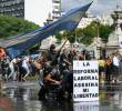 Manifestantes se protegen tras una pancarta que dice “La reforma laboral mata mi libertad” de un cañón de agua disparado por la policía antidisturbios durante una protesta convocada por sindicalistas contra el debate sobre la reforma laboral en el Congreso Nacional en Buenos Aires. FOTO: AFP.