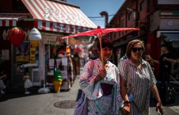 Los turistas comparten un paraguas tradicional para protegerse del sol mientras caminan por una calle comercial en Tokio. FOTO: AFP