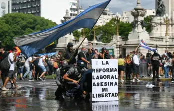 Manifestantes se protegen tras una pancarta que dice “La reforma laboral mata mi libertad” de un cañón de agua disparado por la policía antidisturbios durante una protesta convocada por sindicalistas contra el debate sobre la reforma laboral en el Congreso Nacional en Buenos Aires. FOTO: AFP.