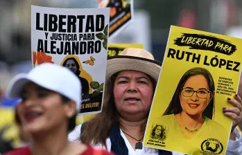 Una mujer lleva fotografías de presos políticos mientras asiste a una protesta contra el Gobierno de Nayib Bukele durante una manifestación. FOTO: AFP