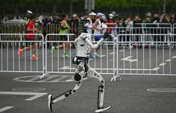 En un carril, uno de los robots humanoides participantes, en el otro, las personas corriendo la media maratón de Pekín. FOTO AFP. 