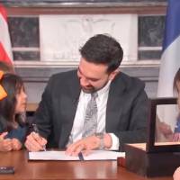 El alcalde de Nueva York, Zohran Mamdani, firma la orden ejecutiva simbólica que “deroga” la hora de dormir de los escolares para las Finales de la NBA, acompañado por niños que estamparon sus huellas en el documento. Foto: Captura de video