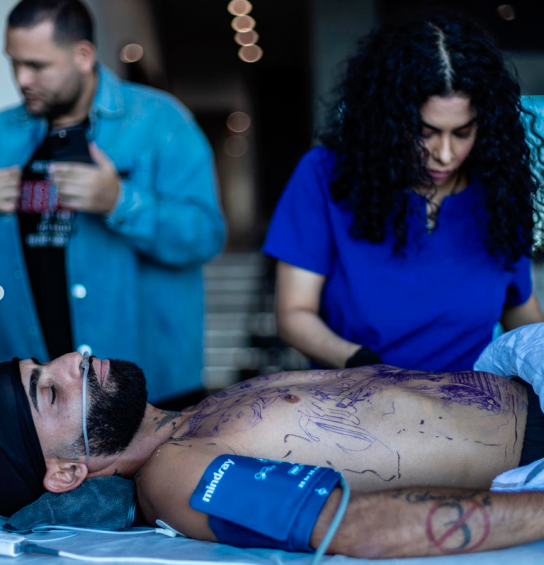 Imagen que Arcángel mientras era tatuado por cinco artistas, que plasmaron sobre su torso una imagen del hermano del músico. FOTO Instagram @arcangel