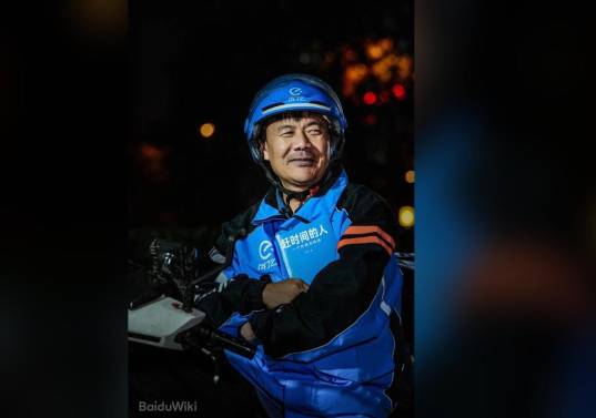 El repartidor chino Wang Jibing, de 56 años, sostiene un ejemplar de su libro de poemas mientras trabaja. En julio de 2026 ganó el Premio Literario Lu Xun, uno de los más importantes de China. / Foto: BaiduWiki 