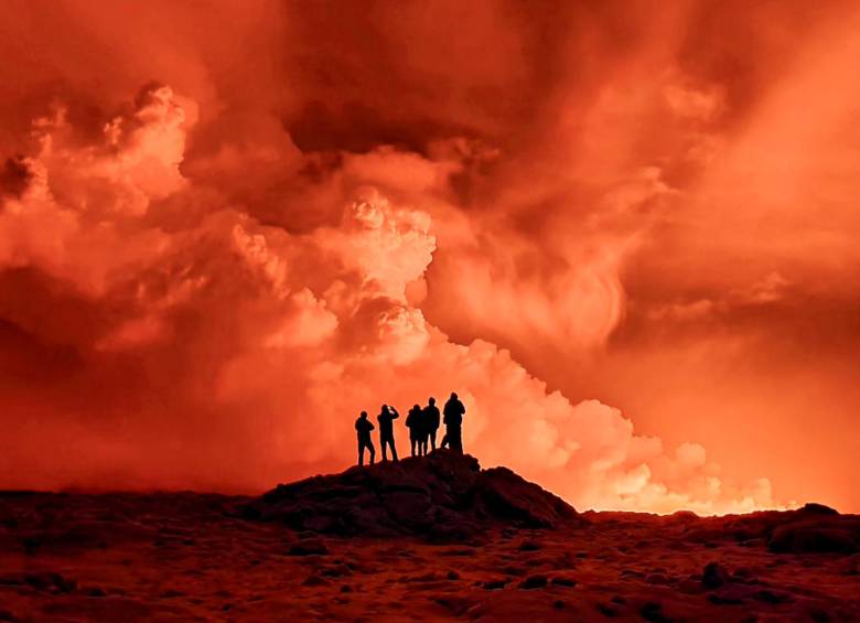 Residentes locales observan cómo se eleva el humo mientras la lava tiñe el cielo nocturno de naranja debido a una erupción volcánica. FOTO AFP