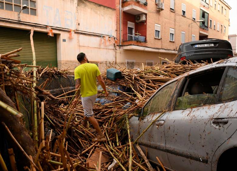 Un hombre camina entre escombros y autos atrapados por las inundaciones. FOTO: AFP