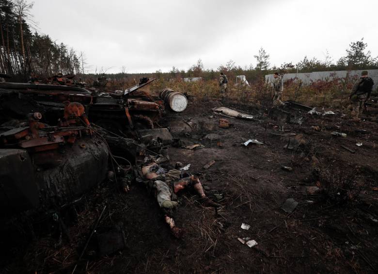 Soldados ucranianos caminan por un campo en el que se ve un tanque quemado y el cuerpo de un soldado ruso. FOTO: EFE.