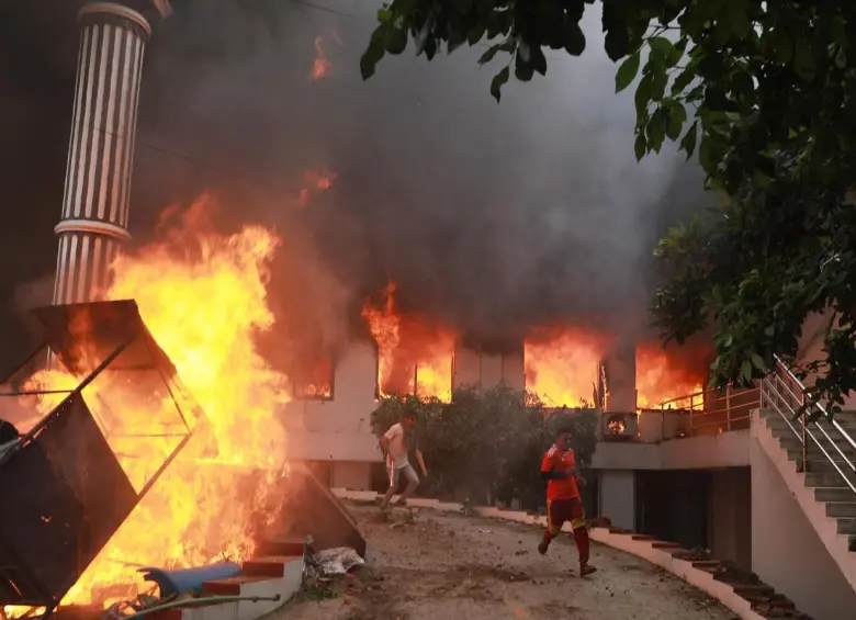 Manifestantes corren junto a las llamas frente a la sede del Partido del Congreso Nepalí incendiada en Katmandú, durante las protestas del 9 de septiembre de 2025 contra la corrupción y la represión policial. FOTO: AFP
