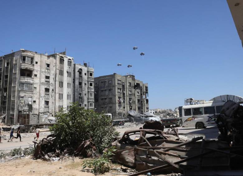 Los palestinos corren hacia paletas de ayuda mientras se lanzan en paracaídas después de ser arrojados desde un avión militar en el norte de la Franja de Gaza. FOTO: AFP