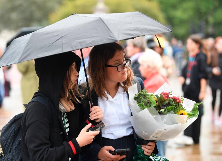 Las personas llegan al Palacio con flores y se cubren con paraguas mientras esperan noticias de la monarca, que lleva 70 años en el trono. FOTO: EFE