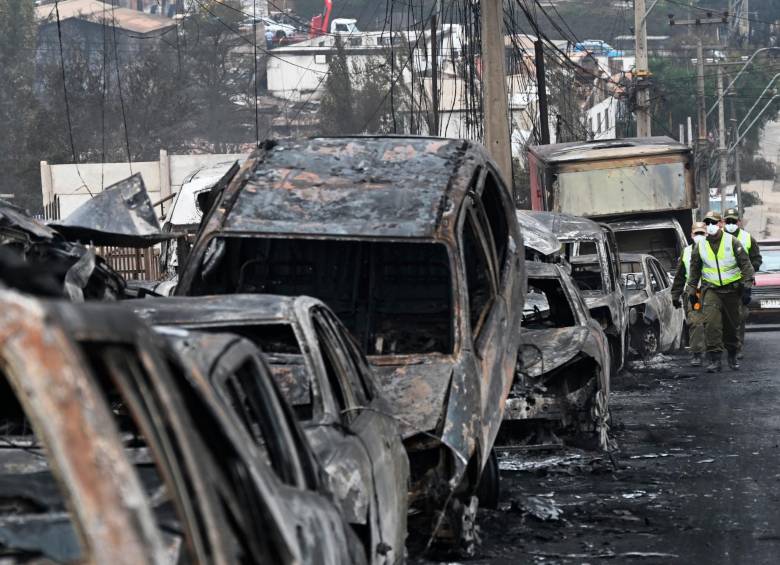 Carabineros chilenos pasan junto a vehículos quemados tras incendio forestal en Quilpue. FOTO AFP