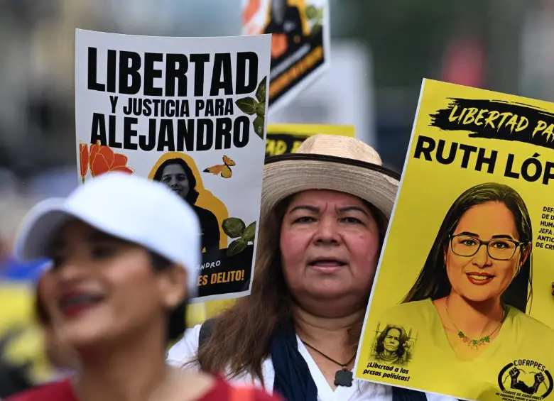 Una mujer lleva fotografías de presos políticos mientras asiste a una protesta contra el Gobierno de Nayib Bukele durante una manifestación. FOTO: AFP