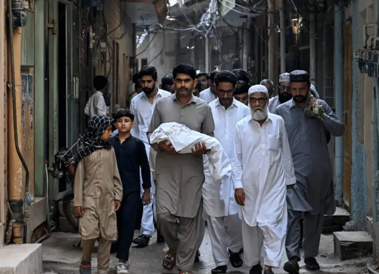 Un hombre carga el cuerpo de un recién nacido que murió tras el incendio en Pakistán. Foto: AFP.