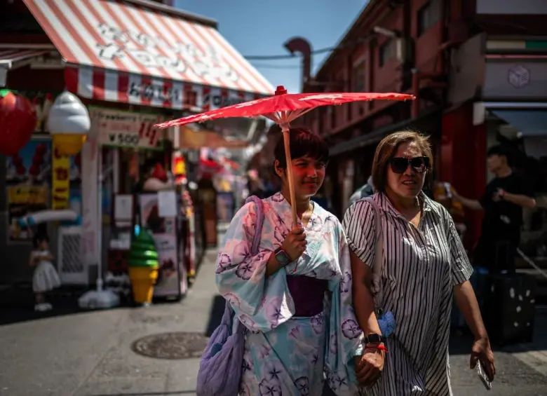 Los turistas comparten un paraguas tradicional para protegerse del sol mientras caminan por una calle comercial en Tokio. FOTO: AFP