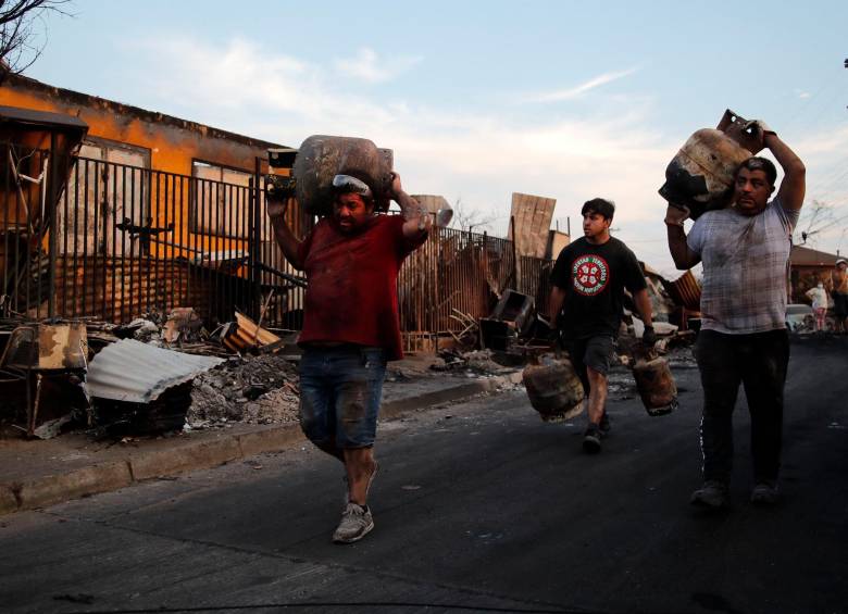 Sobrevivientes cargan galones de gasolina después de un incendio forestal en Villa Independencia, región de Valparaíso. FOTO AFP