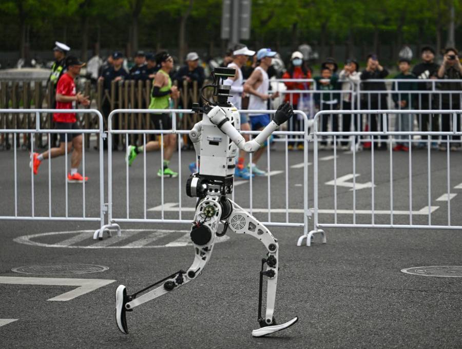 En un carril, uno de los robots humanoides participantes, en el otro, las personas corriendo la media maratón de Pekín. FOTO AFP. 