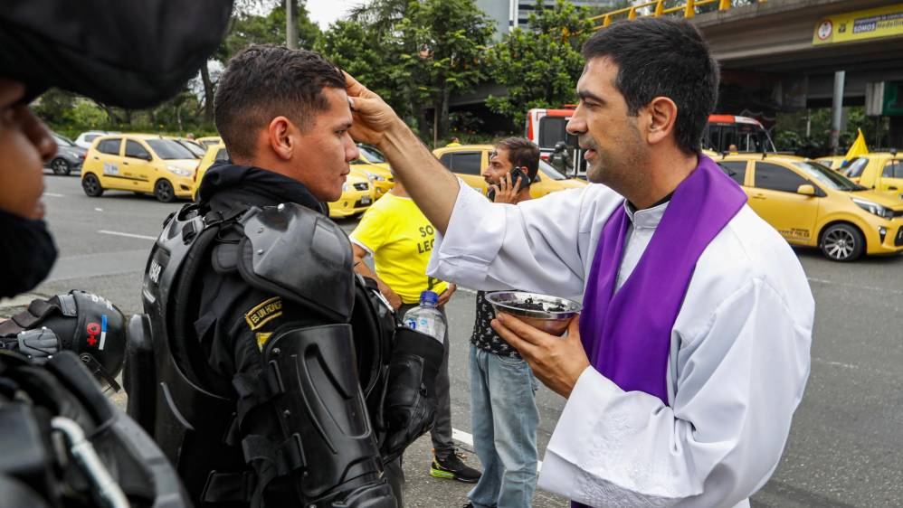  Mientras cumplen con su labor de mantener el orden en la ciudad el presbítero Juan Felipe Escobar impone la ceniza a miembros del Esmad. Foto: MANUEL SALDARRIAGA QUINTERO.
