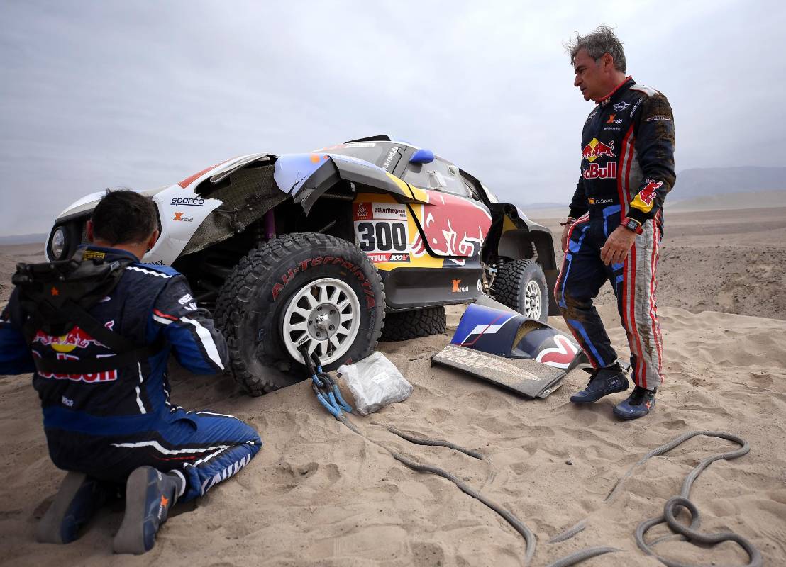 El piloto español de Mini, Carlos Sainz (R) y su copiloto Lucas Cruz, se arrodillan junto a su automóvil luego de que la suspensión delantera de su Mini se rompió durante la Etapa 3 del Rally Dakar entre San Juan de Marcona y Arequipa. Foto: AFP