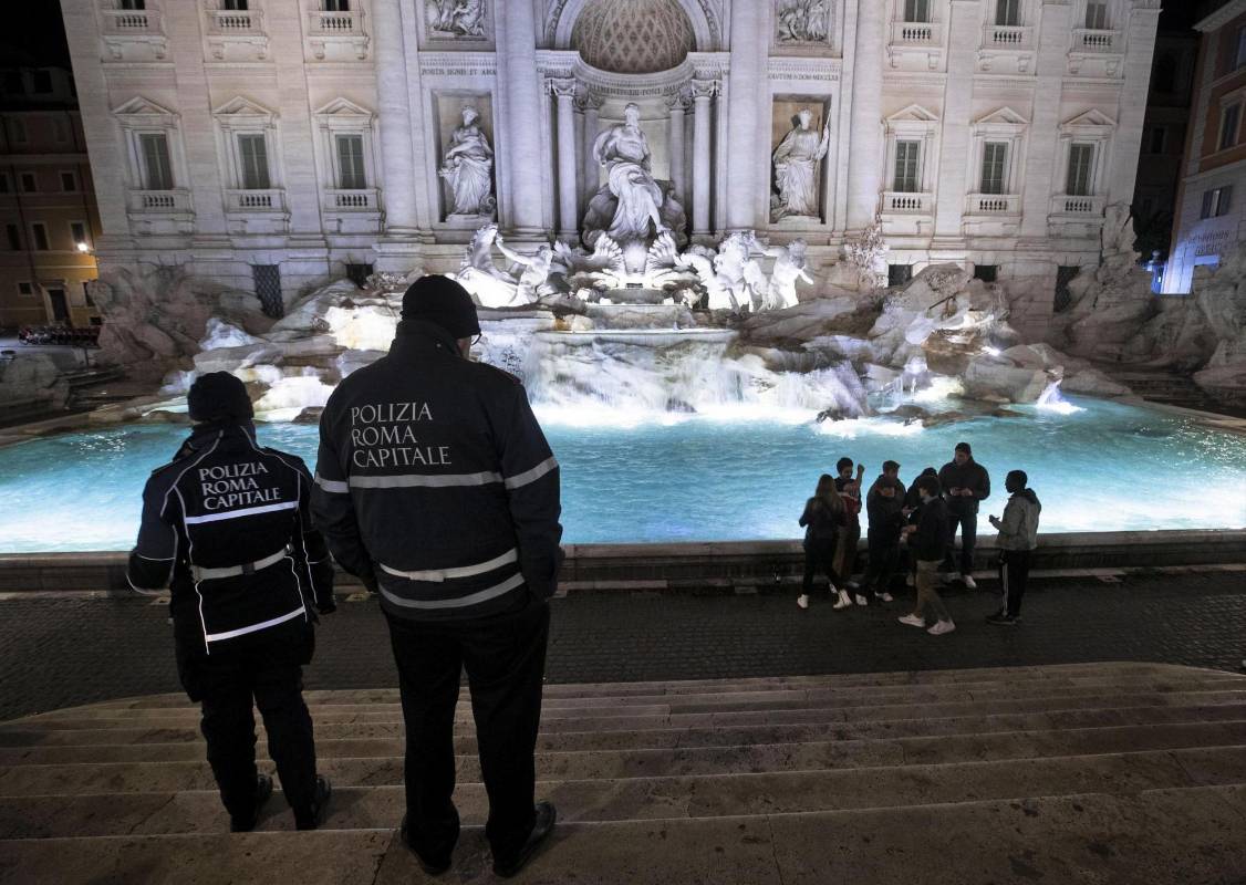 En la noche del domingo, dos policías vigilaban a un grupo de jóvenes que quebrantaba el aislamiento en Roma. Las personas sorprendidas en las calles se exponen a multas o al arresto. FOTO EFE