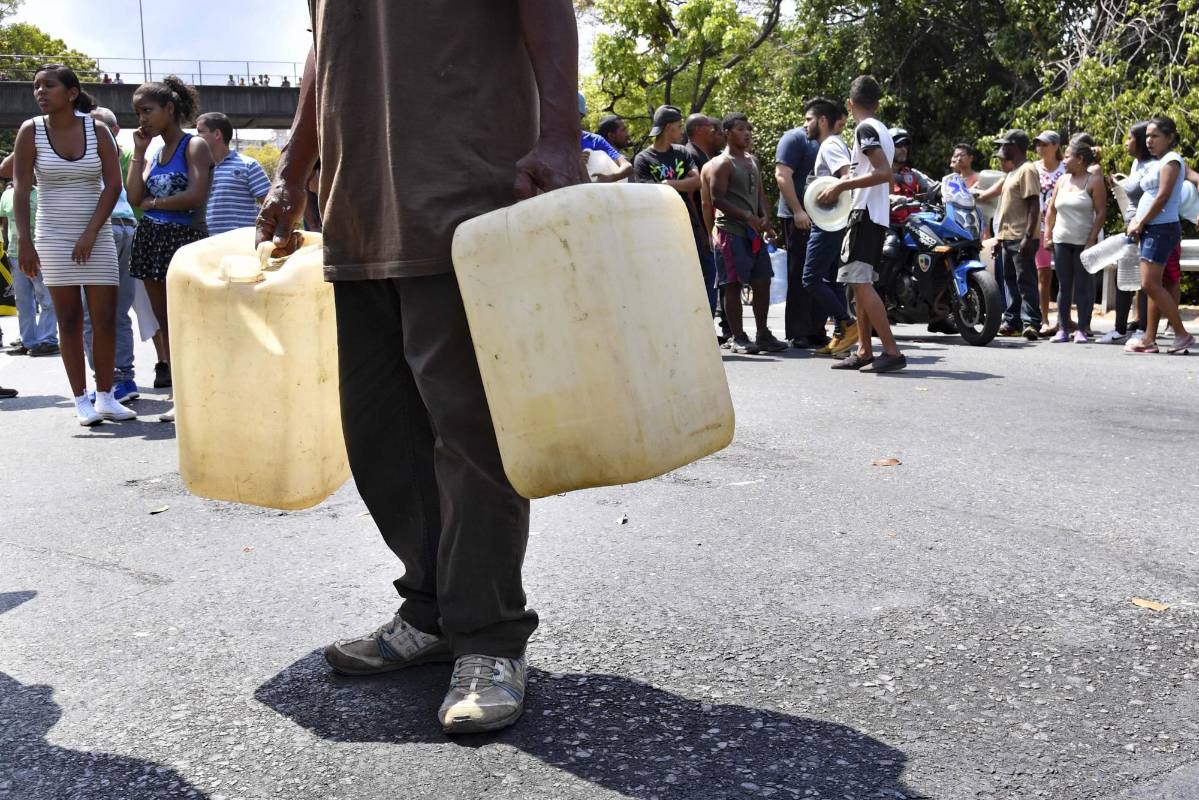 Las personas con latas y cubos esperan a recolectar agua de un canal de aguas residuales en el río Guaire en Caracas, mientras un apagón masivo continúa afectando algunas áreas del país. Foto: Yuri Cortez