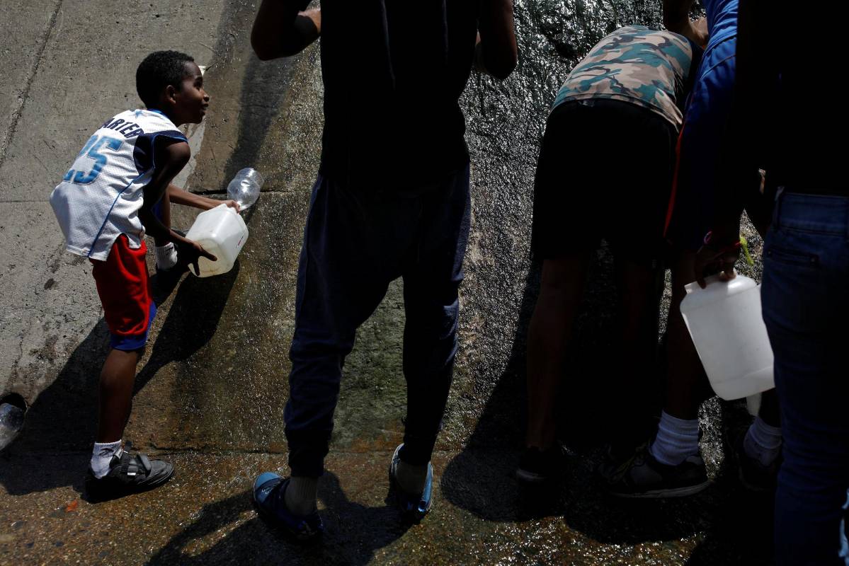 La gente recolecta agua de un canal de aguas residuales en el río Guaire en Caracas, mientras un apagón masivo continúa afectando algunas áreas del país. Foto: Carlos García Rawlins