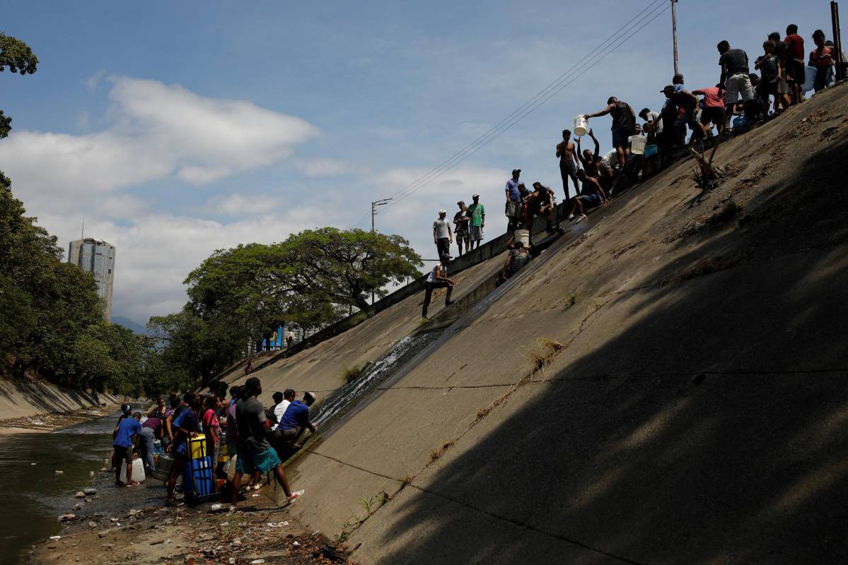 La gente recolecta agua de un canal de aguas residuales en el río Guaire en Caracas, mientras un apagón masivo continúa afectando algunas áreas del país. Foto: Carlos García Rawlins
