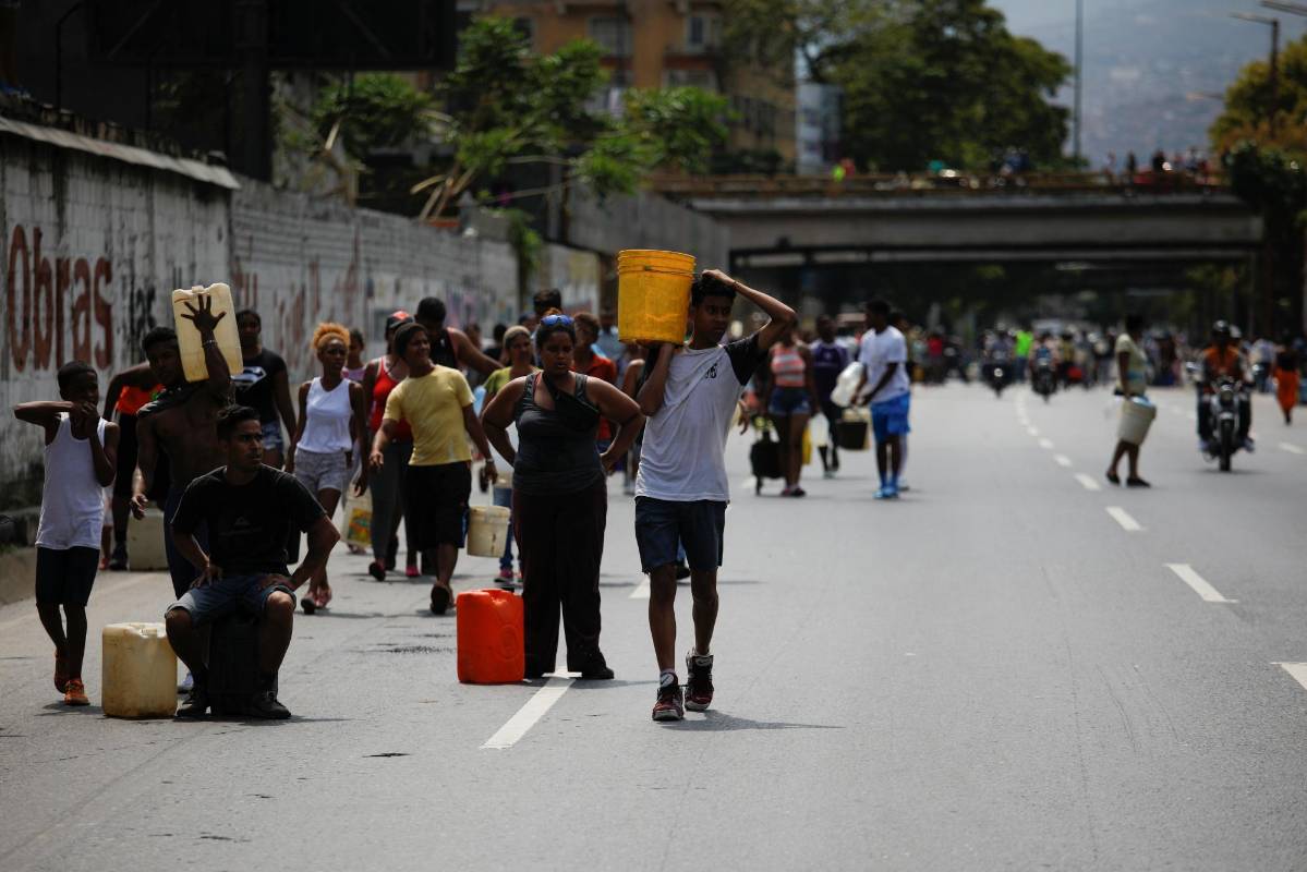 Las personas con latas y cubos esperan a recolectar agua de un canal de aguas residuales en el río Guaire en Caracas, mientras un apagón masivo continúa afectando algunas áreas del país. Foto: Carlos García Rawlins