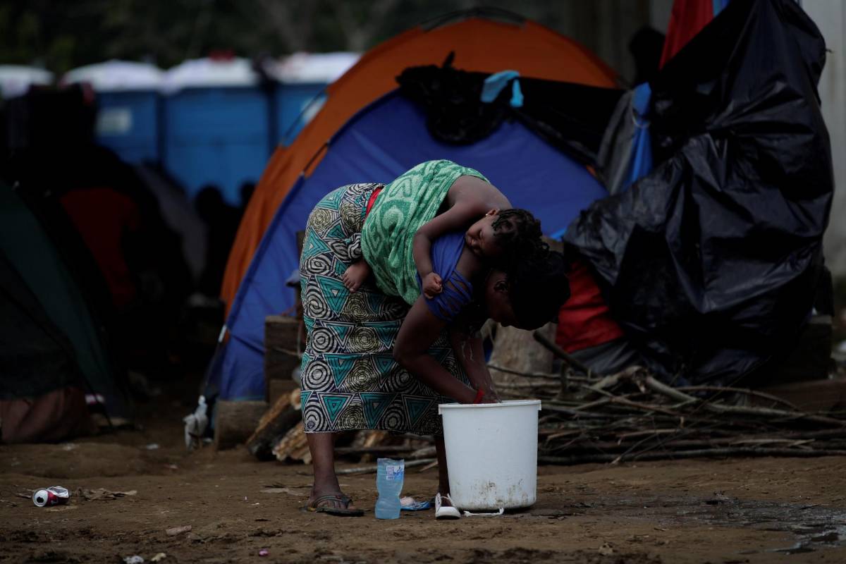 Una mujer migrante carga a su hija mientras lava platos el pasado 22 de mayo 2019, en una estación temporal de ayuda humanitaria en la comunidad de Peñita, en Darién (Panamá).