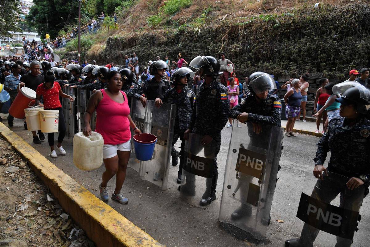 Las personas con latas y cubos esperan a recolectar agua de un canal de aguas residuales en el río Guaire en Caracas, mientras un apagón masivo continúa afectando algunas áreas del país. Foto: Yuri Cortez